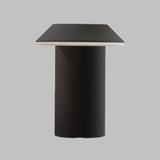 A modern table lamp with a matte black cylindrical base and a tapered square shade in a dark charcoal gray, featuring a thin white accent rim, shown against a solid gray background.