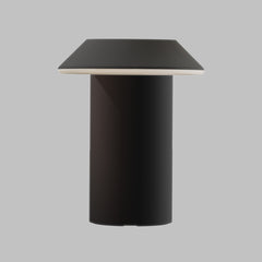 A modern table lamp with a matte black cylindrical base and a tapered square shade in a dark charcoal gray, featuring a thin white accent rim, shown against a solid gray background.