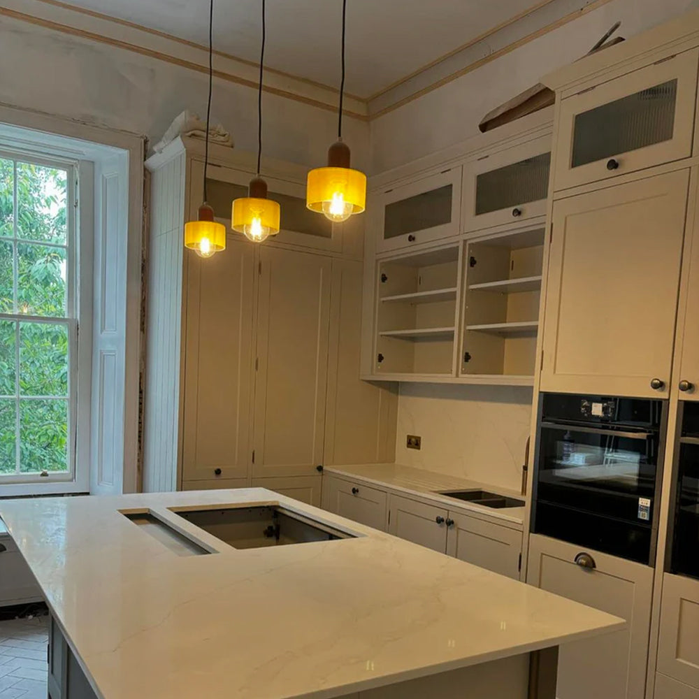 Three mini glass pendant lights lit above a white kitchen island