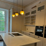 Three mini glass pendant lights lit above a white kitchen island