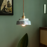 Pale green stepped ceramic pendant lit against a green wall