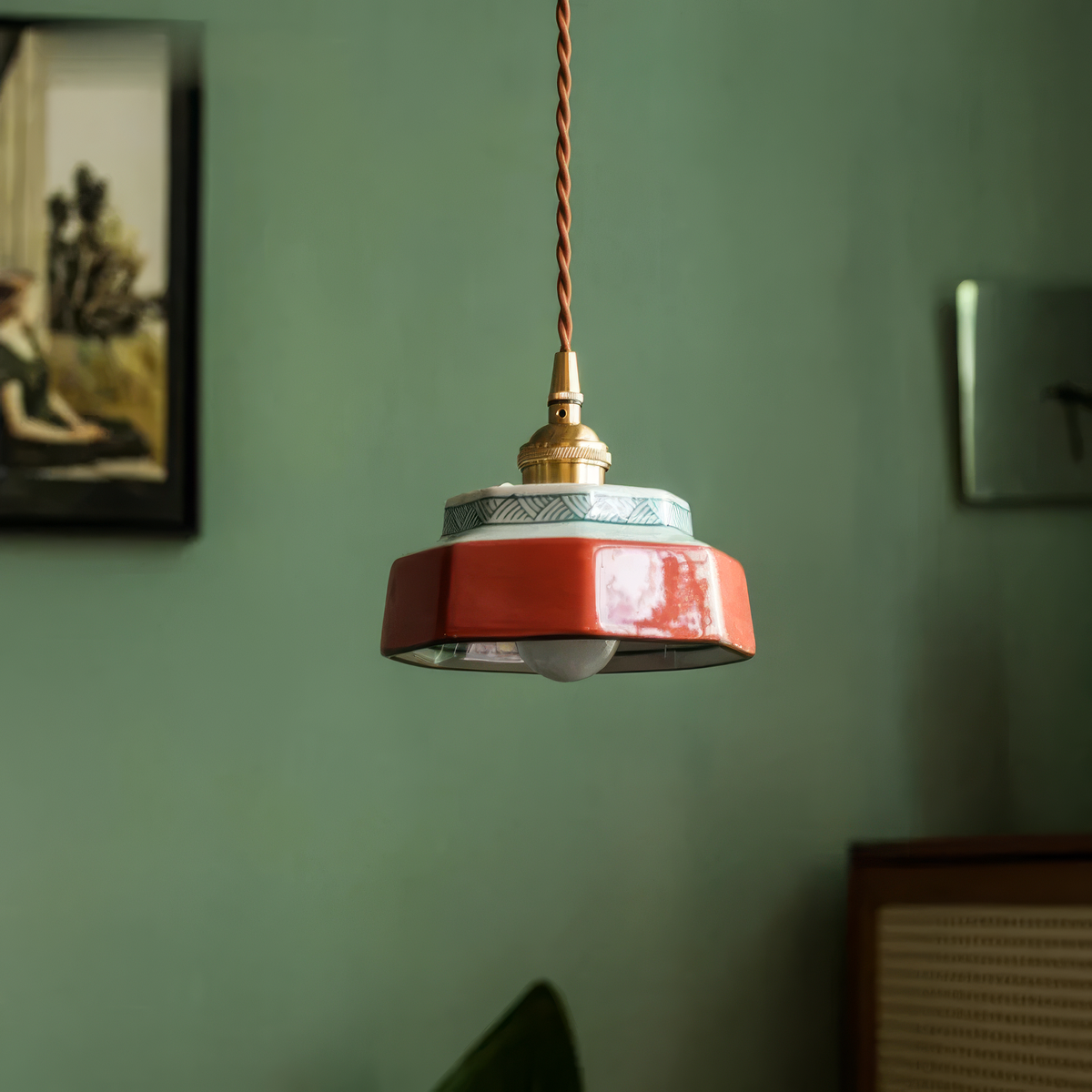 Terracotta stepped ceramic pendant lit against a green wall