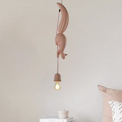 Pink squirrel pendant lit against a plain wall beside a cushion