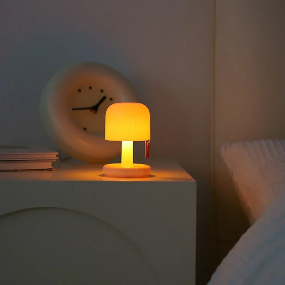 Mini rechargeable table lamp lit on a bedside table beside a round clock