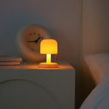Mini rechargeable table lamp lit on a bedside table beside a round clock