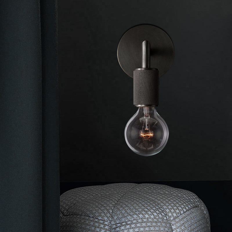 Black sconce lit above a gray knitted pouffe in a dark room