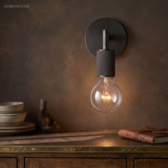 Black wall sconce lit warm on a rust colored wall above a sideboard