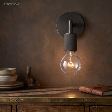 Black wall sconce lit warm on a rust colored wall above a sideboard