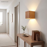 Wood cube wall sconce lit on a white wall beside a console table