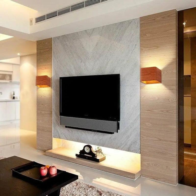 Two wood cube sconces lit on a marble wall beside a television