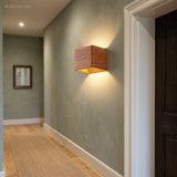 Wood cube wall sconce lit on a green hallway wall