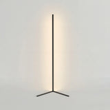 Black corner floor lamp on a triangle base with warm glow on a plain wall