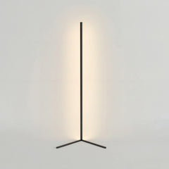Black corner floor lamp on a triangle base with warm glow on a plain wall