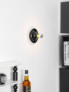 Black disc wall sconce viewed at an angle above bottles on a cabinet