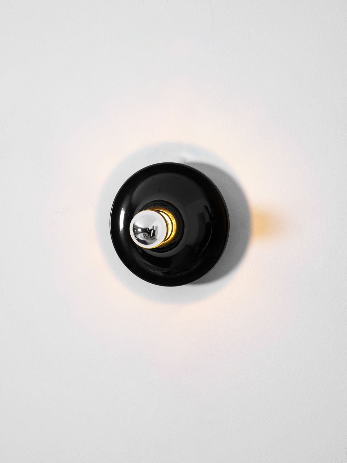 Black disc wall sconce face on with a warm glow around the rim