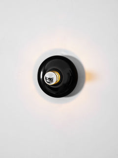 Black disc wall sconce face on with a warm glow around the rim