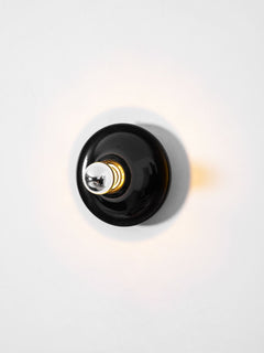 Black disc wall sconce face on lit with warm light on the wall