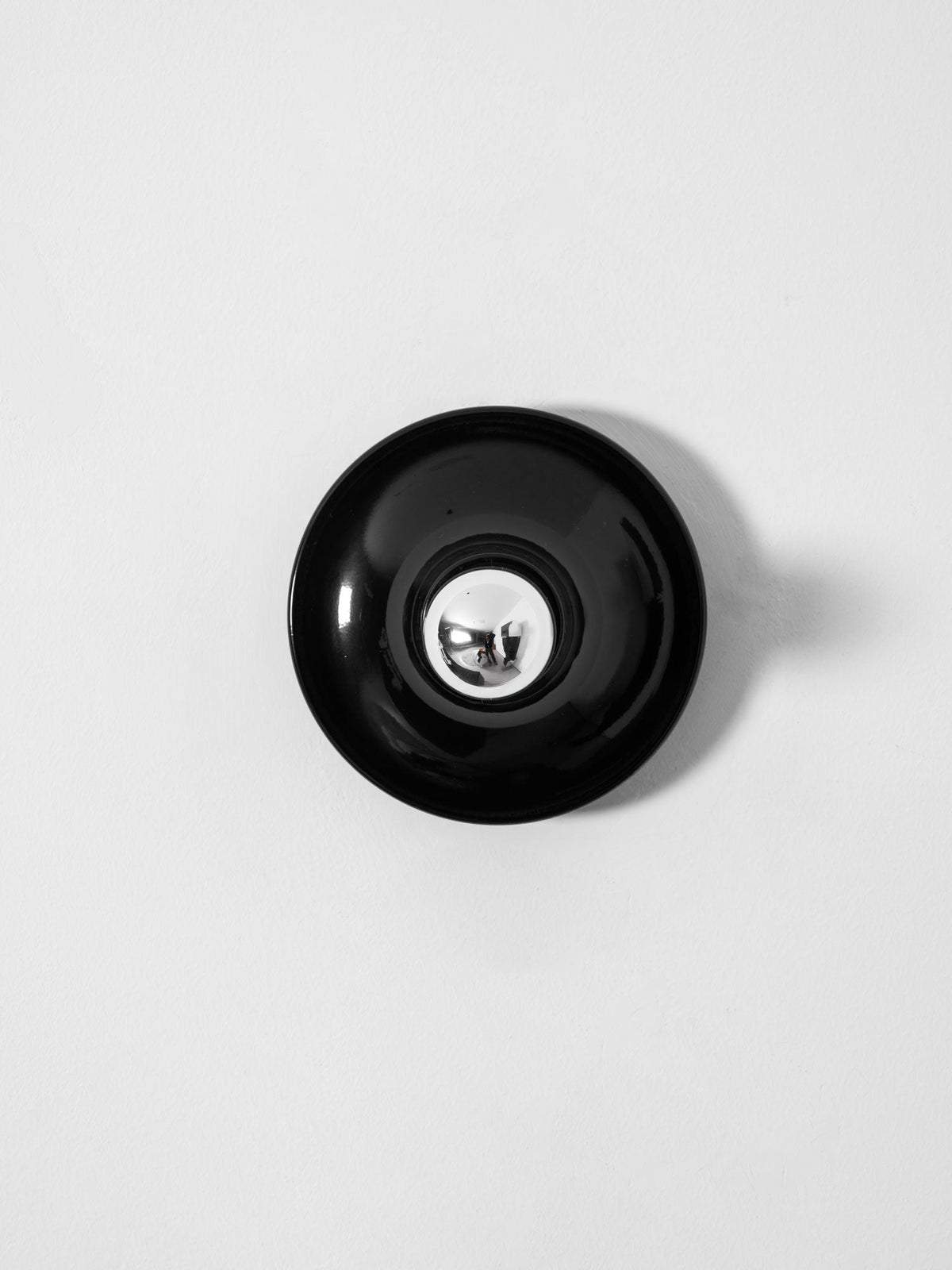 Black disc wall sconce face on unlit showing the mirrored bulb crown