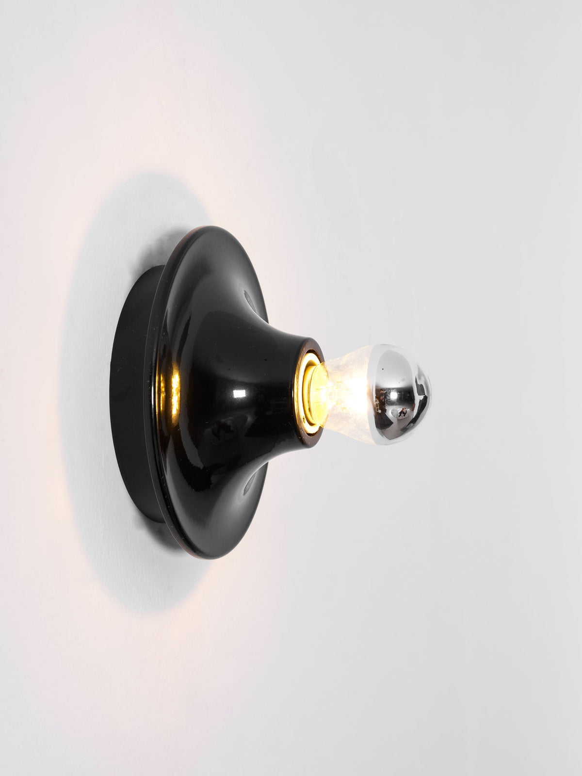 Black disc wall sconce side view with a lit mirror crown bulb