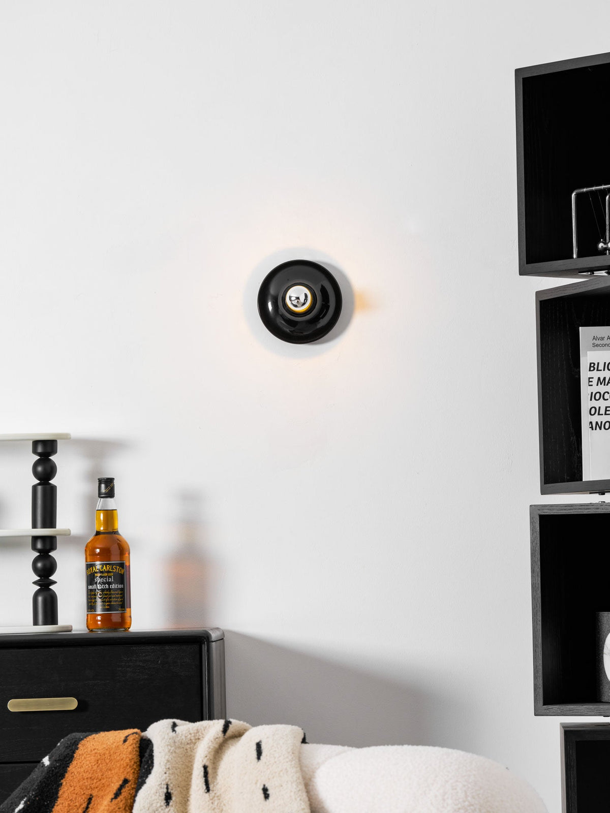 Black disc wall sconce in a room with black shelving and a sculpture