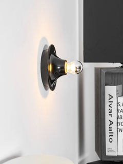 Black disc wall sconce glowing warmly next to a dark book shelf