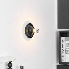 Black disc sconce lit on a white wall beside dark bookshelves