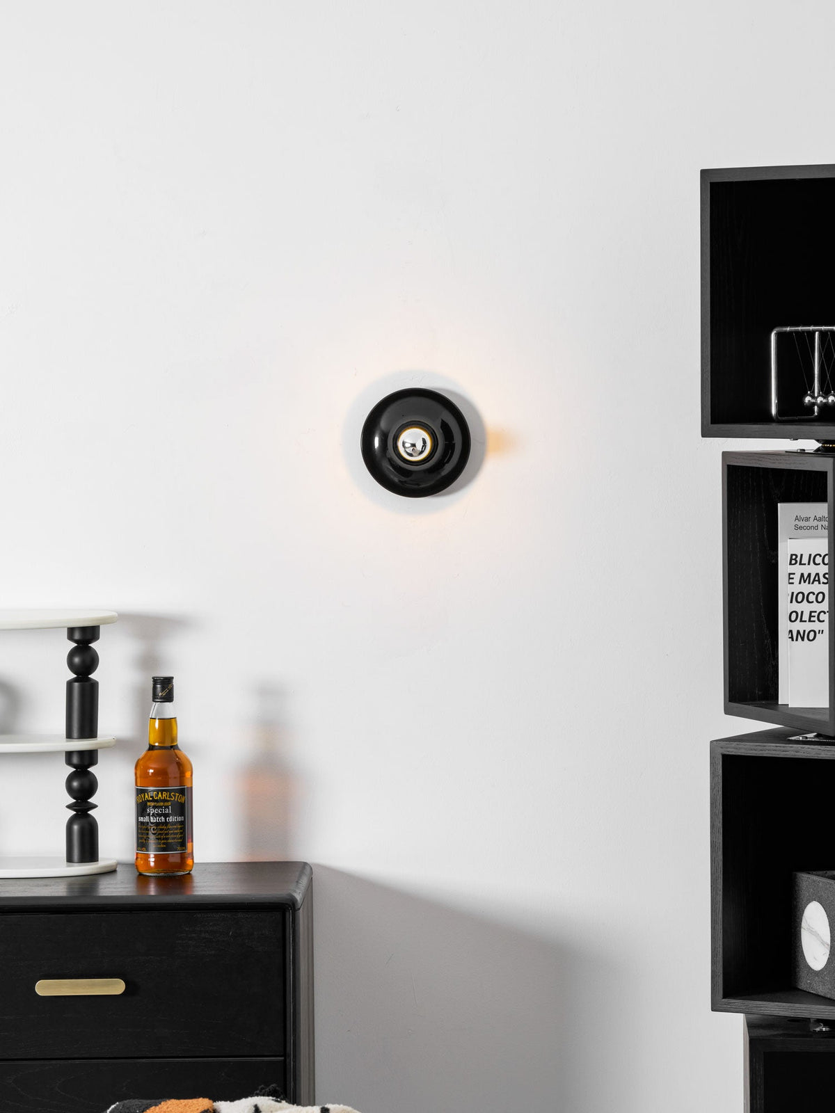 Black disc wall sconce on a white wall beside a black shelving unit