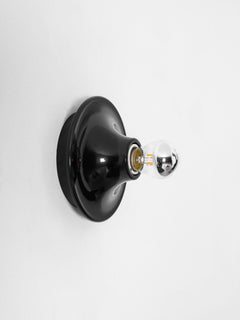 Black disc wall sconce side profile against a plain white wall