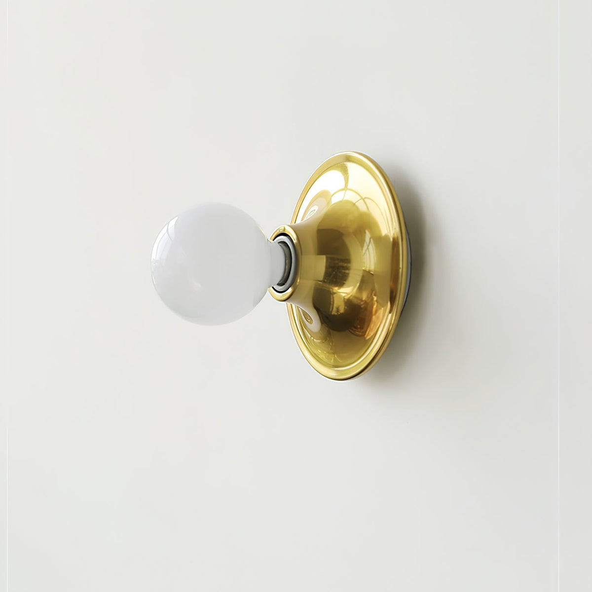 Brass disc wall sconce with an opal white globe bulb, angled view