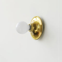 Brass disc wall sconce with an opal white globe bulb, angled view
