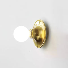 Brass disc wall sconce with a glowing opal white globe bulb