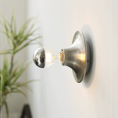 Nickel disc sconce with a mirror crown electroplated bulb beside a green plant