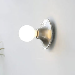 Nickel disc wall sconce with a lit opal globe bulb on a white wall