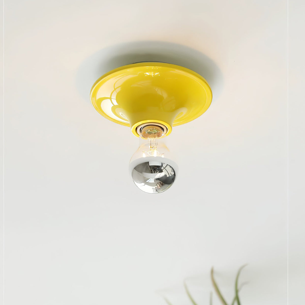 Yellow disc ceiling light with an electroplated bulb above a leafy plant