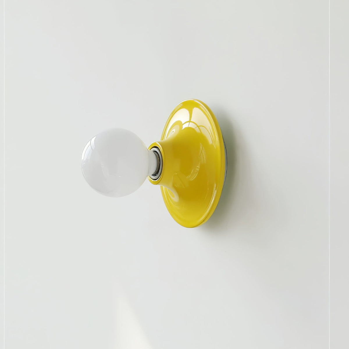 Yellow disc wall sconce seen from an angle with an opal globe bulb