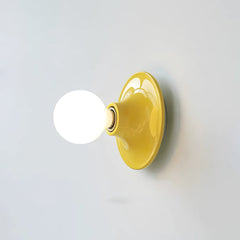 Yellow disc wall sconce with a lit opal globe bulb on white