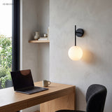 Black stem globe sconce lit on a plaster wall above a timber desk and laptop