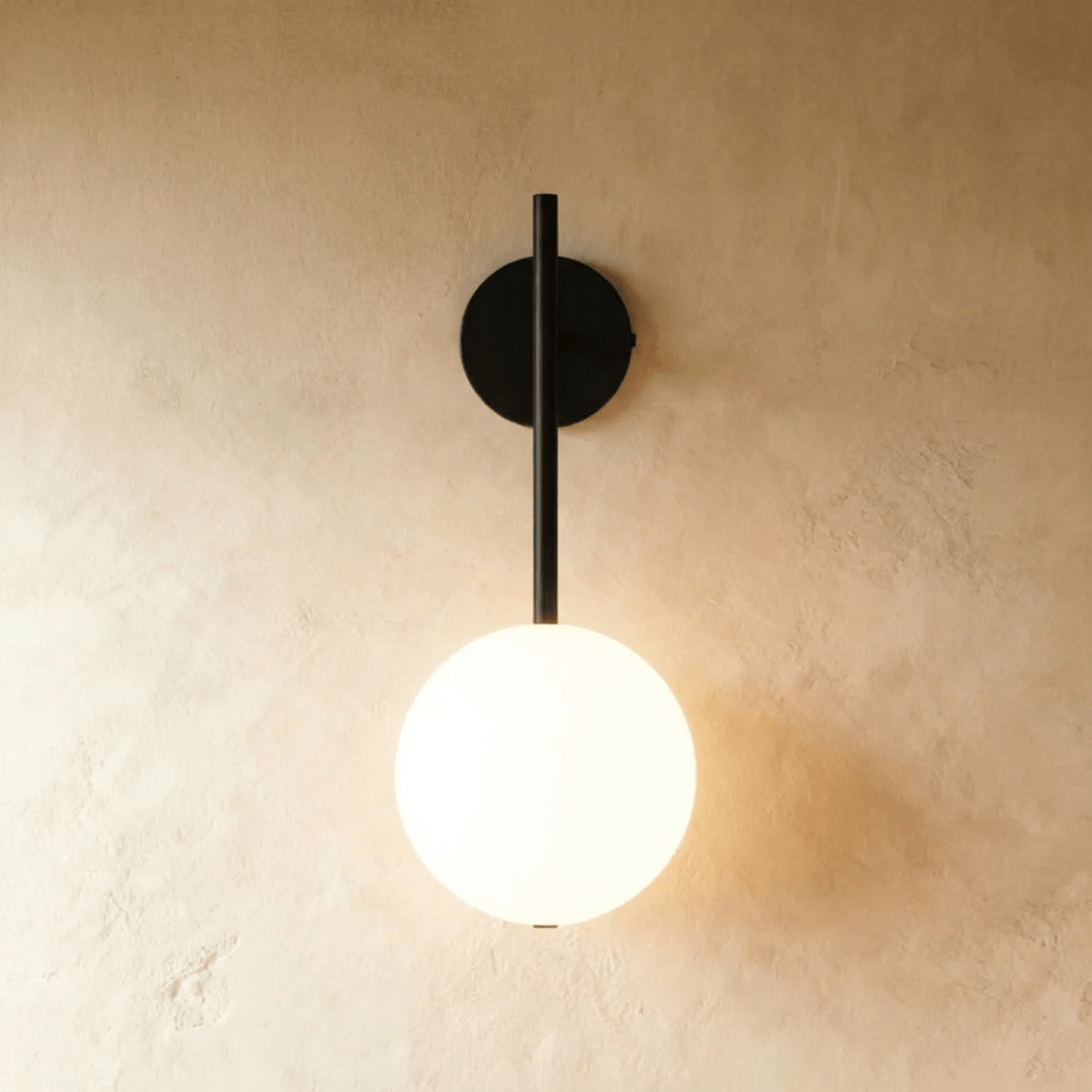 Gold stem sconce with lit glass globe against a warm textured plaster wall