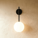 Gold stem sconce with lit glass globe against a warm textured plaster wall
