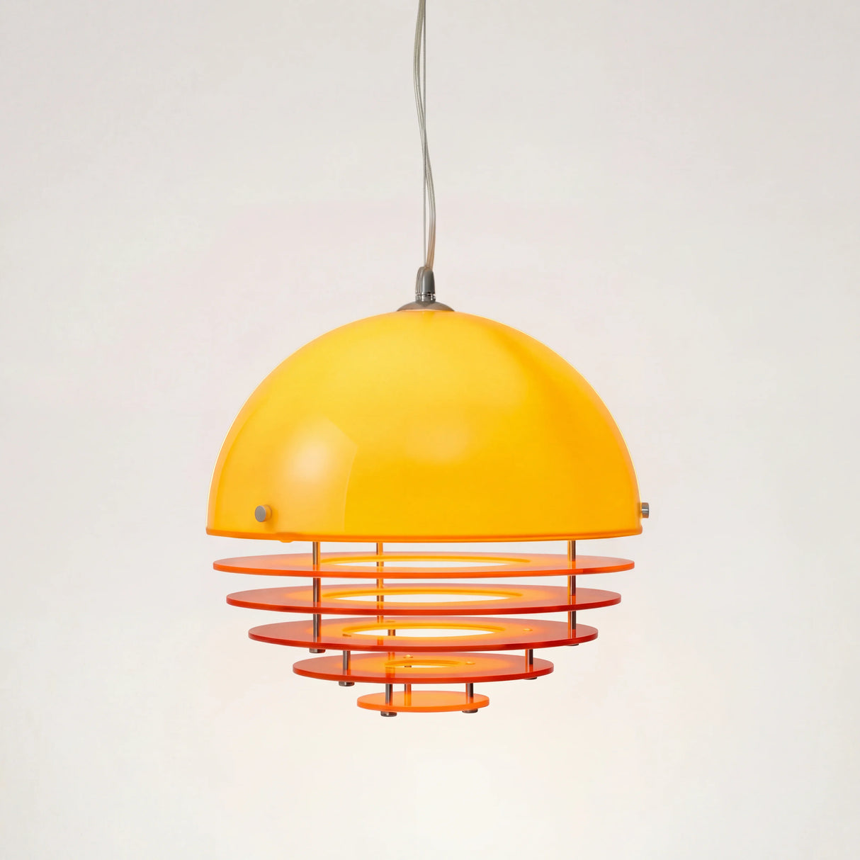 Orange glass dome pendant light with layered rings on a plain studio background