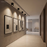 Row of black ceiling spotlights lighting framed prints along a corridor