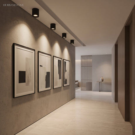 Row of black ceiling spotlights lighting framed prints along a corridor