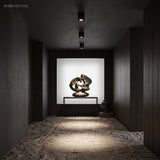 Black surface mount spotlights lighting a bronze sculpture in dark hallway