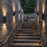 Black up down wall sconces lit along a stone wall beside outdoor steps