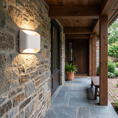 White up down wall sconce lit on a stone wall along a covered walkway