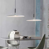 Two saucer pendants lit above a dining table beside a green wall