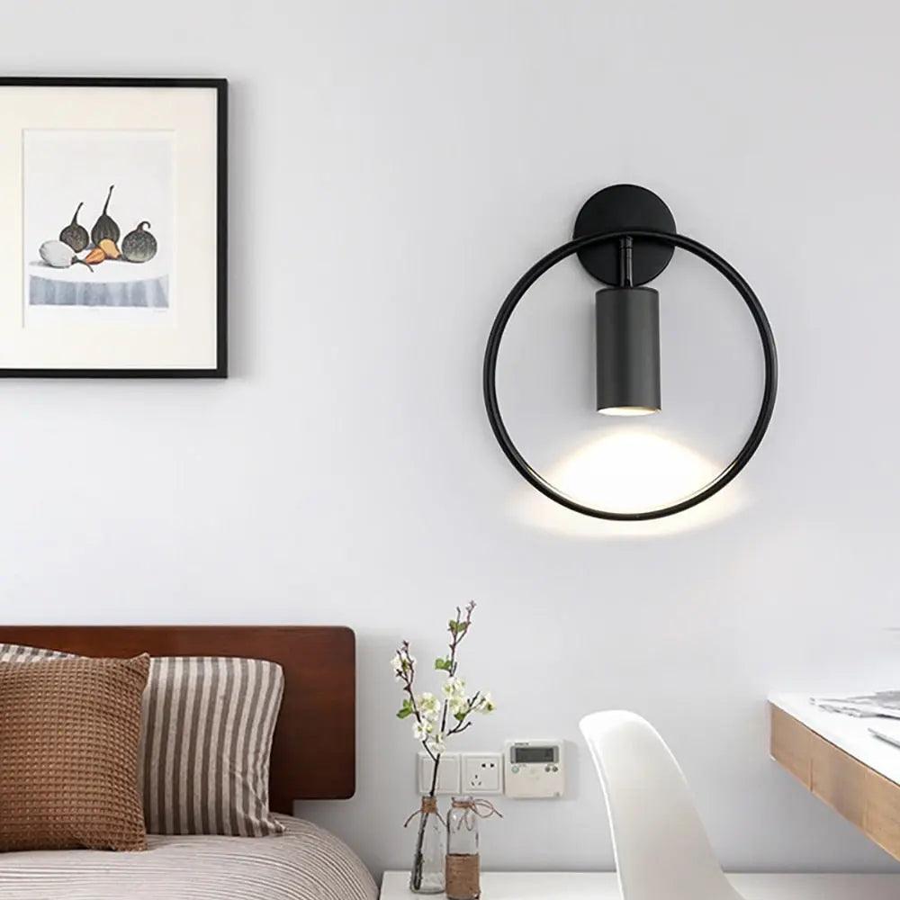 Black ring sconce on a white wall beside framed art and a chair