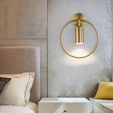 Gold ring sconce lit above a bed with a pale upholstered headboard