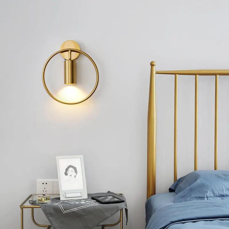 Gold hoop sconce beside a brass bed frame and bedside table