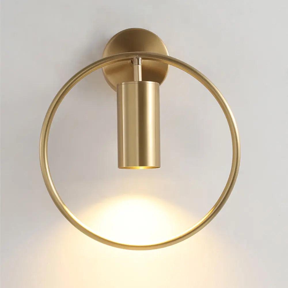 Gold ring and cylinder sconce lit against a plain pale wall